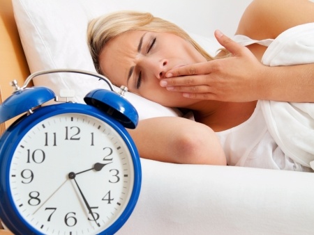 Sleepy woman yawning in bed next to alarm clock