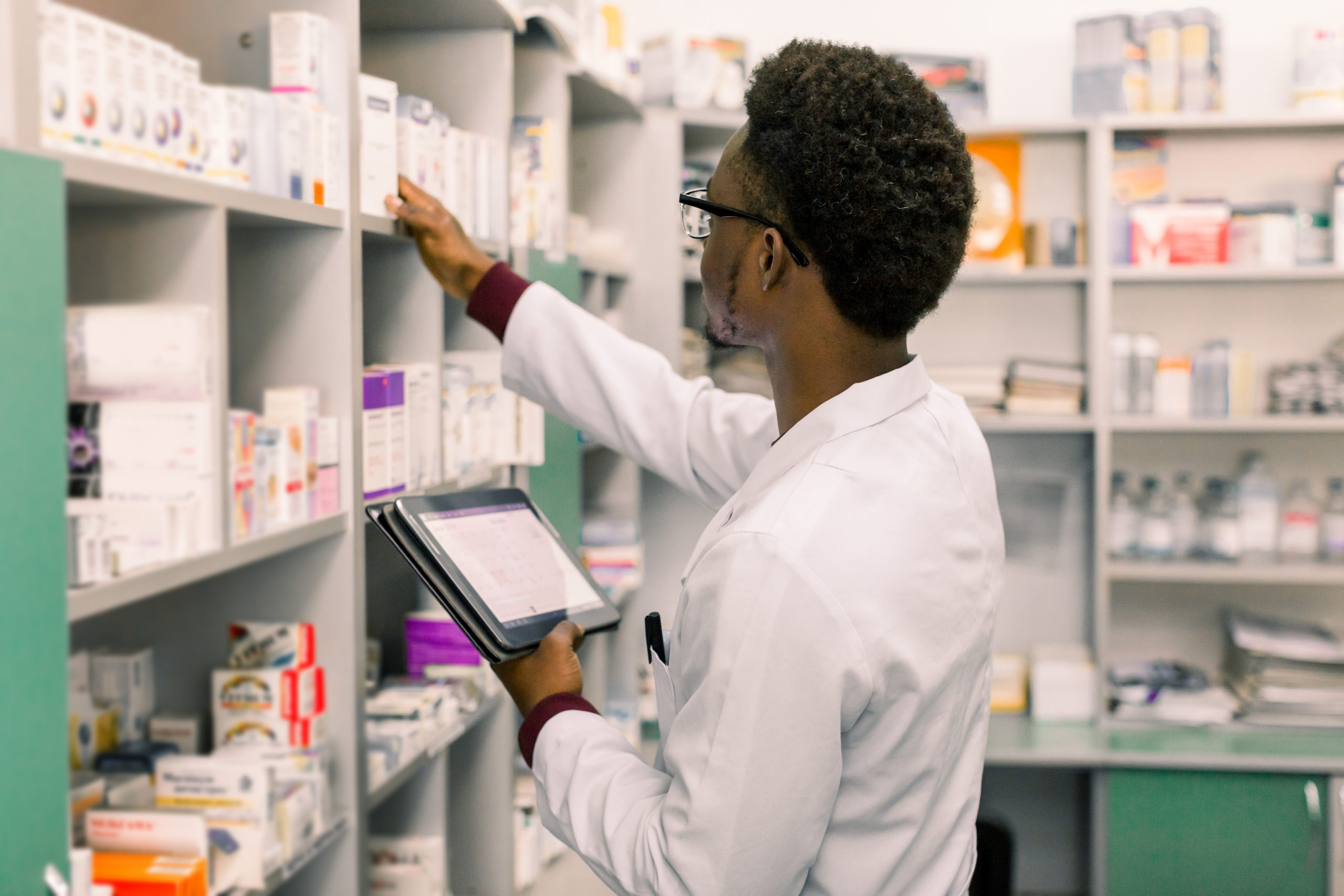 male pharmacist taking medication off shelf to fill prescription
