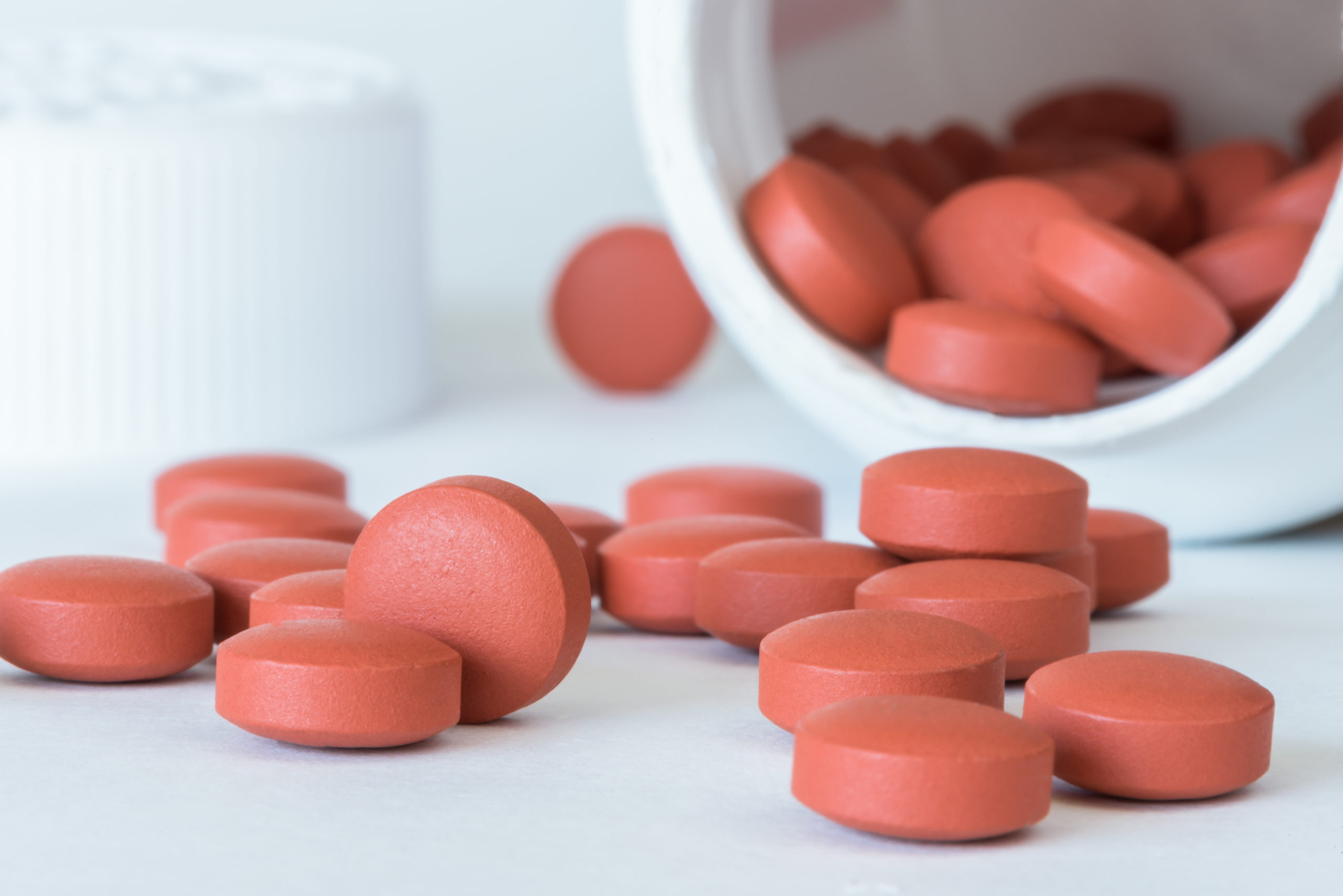 open bottle of ibuprofen tipped sideways spilling pills on a white table