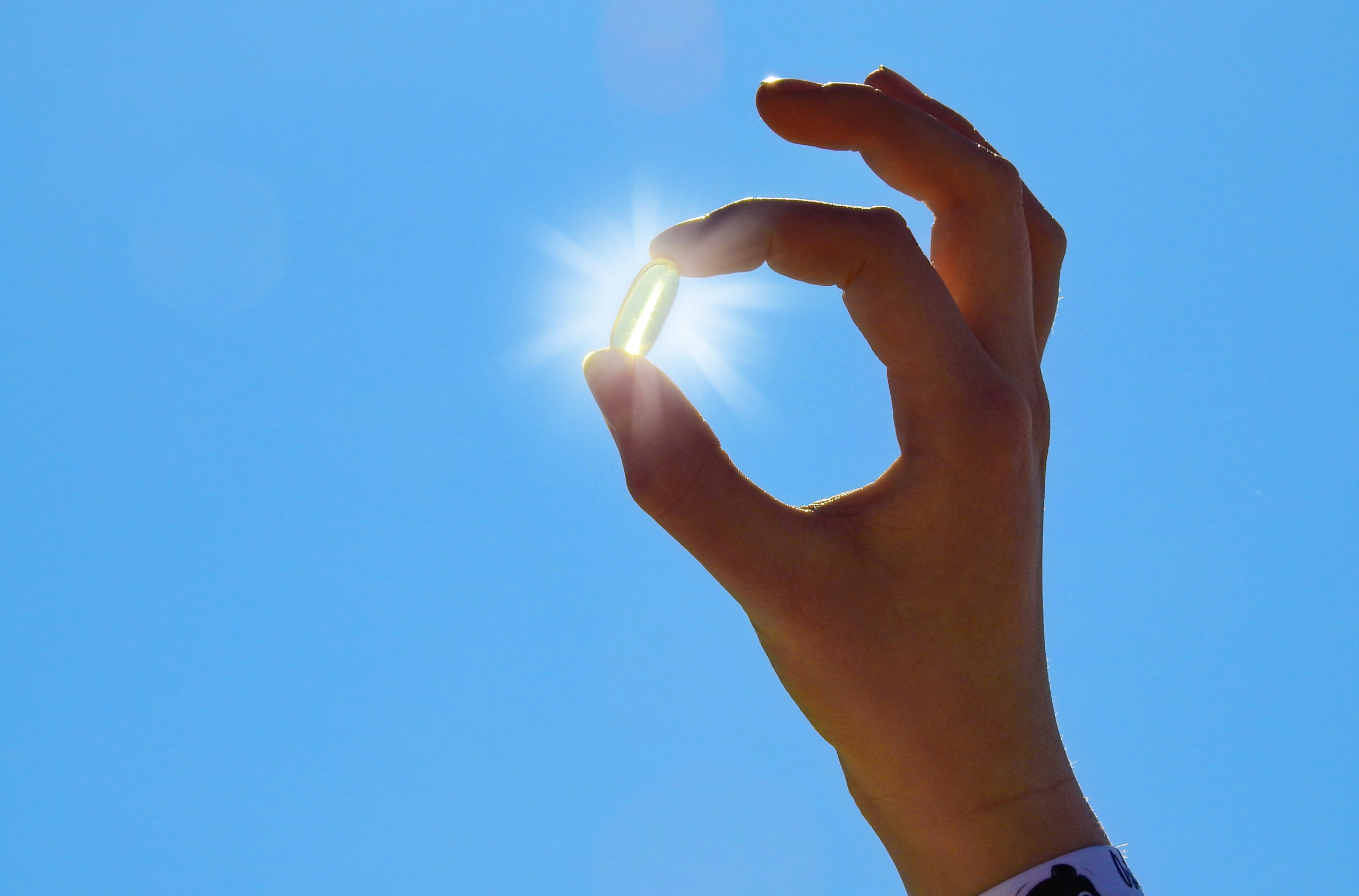 hand holding vitamin D pill up in front of the sun with blue background
